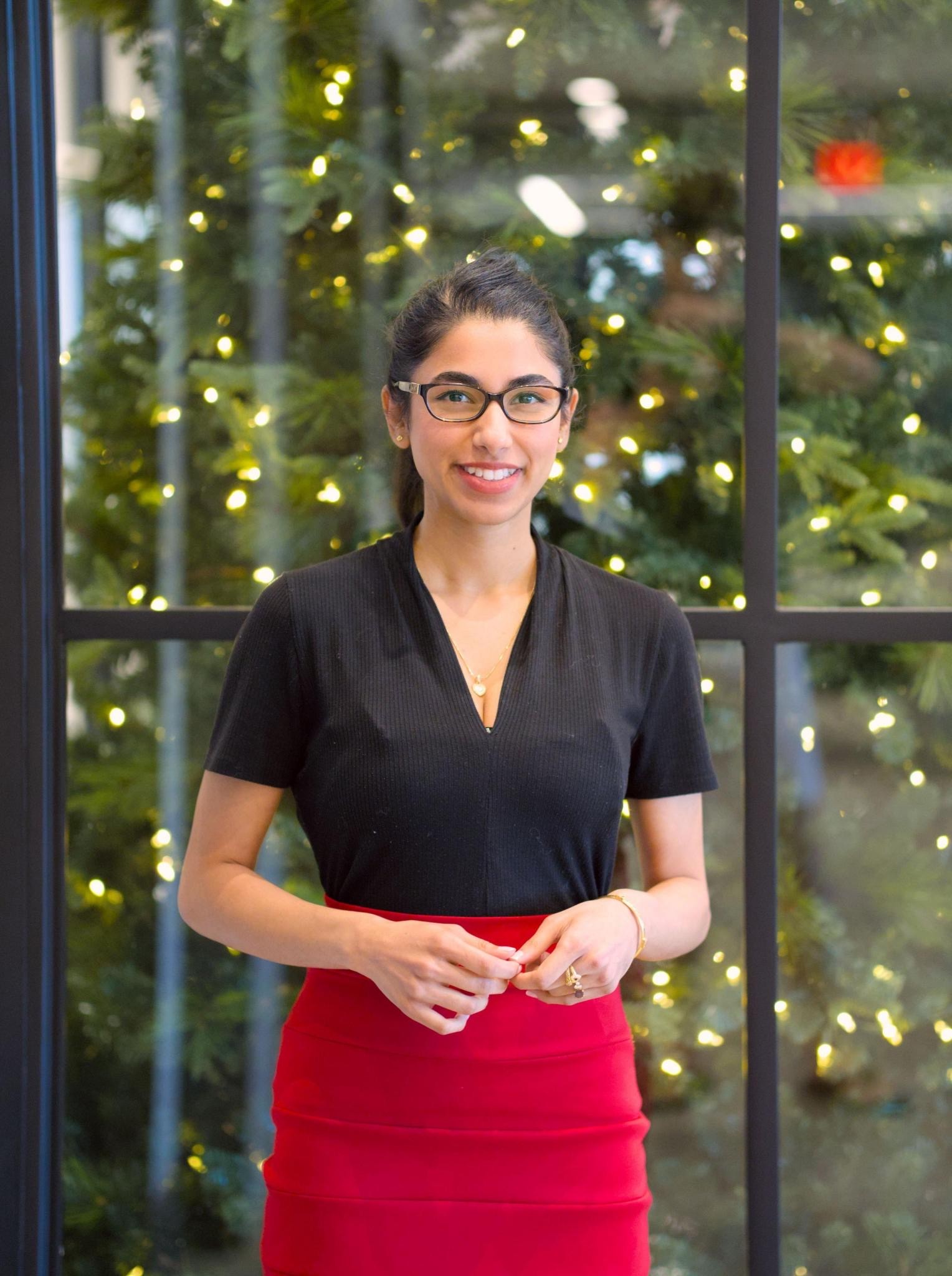 Photo of UT student standing in front of a window with a large tree.